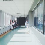 Corredor hospitalar bem iluminado, com profissionais de saúde usando jalecos ao fundo.