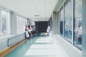 Corredor hospitalar bem iluminado, com profissionais de saúde usando jalecos ao fundo.