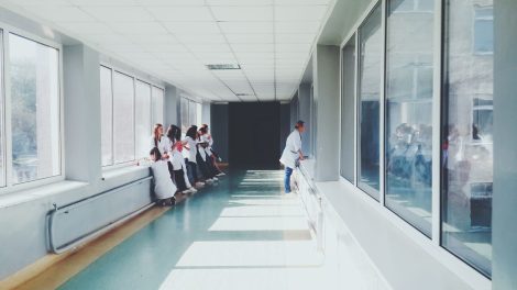 Corredor hospitalar bem iluminado, com profissionais de saúde usando jalecos ao fundo.