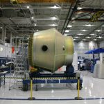 Equipamento espacial em construção sobre uma plataforma móvel dentro de uma fábrica aeroespacial.