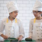 Duas crianças usando aventais e preparando vegetais em uma cozinha.