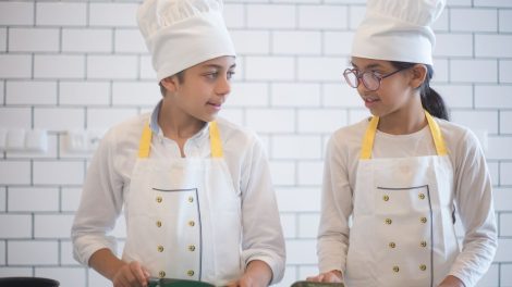 Duas crianças usando aventais e preparando vegetais em uma cozinha.