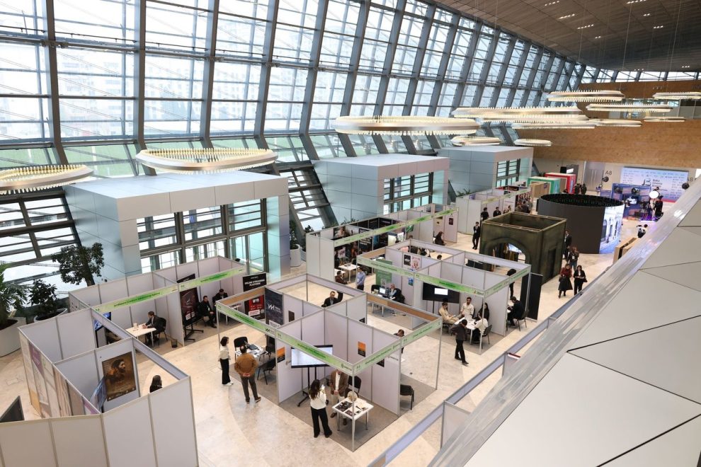 Pessoas circulam e conversam entre estandes de uma feira de negócios em um pavilhão moderno.