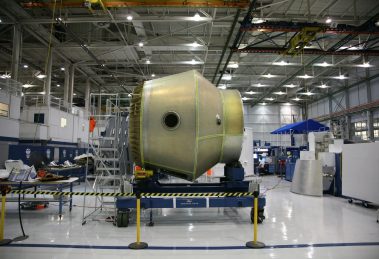 Equipamento espacial em construção sobre uma plataforma móvel dentro de uma fábrica aeroespacial.