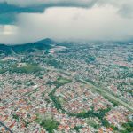 Vista aérea de uma extensa área urbana e de morros verdes sob a aproximação de uma tempestade.