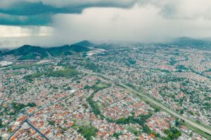 Vista aérea de uma extensa área urbana e de morros verdes sob a aproximação de uma tempestade.
