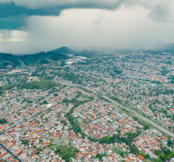 Vista aérea de uma extensa área urbana e de morros verdes sob a aproximação de uma tempestade.