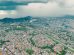 Vista aérea de uma extensa área urbana e de morros verdes sob a aproximação de uma tempestade.