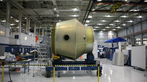 Equipamento espacial em construção sobre uma plataforma móvel dentro de uma fábrica aeroespacial.