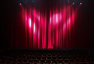 Palco de teatro vazio, com cortinas vermelhas e assentos ao fundo, preparado para uma apresentação.