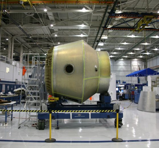 Equipamento espacial em construção sobre uma plataforma móvel dentro de uma fábrica aeroespacial.