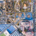 Vista aérea de um parque urbano com áreas de lazer, estacionamento e prédios ao redor