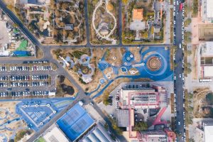 Vista aérea de um parque urbano com áreas de lazer, estacionamento e prédios ao redor