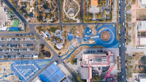 Vista aérea de um parque urbano com áreas de lazer, estacionamento e prédios ao redor