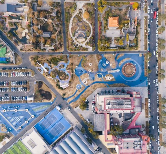 Vista aérea de um parque urbano com áreas de lazer, estacionamento e prédios ao redor