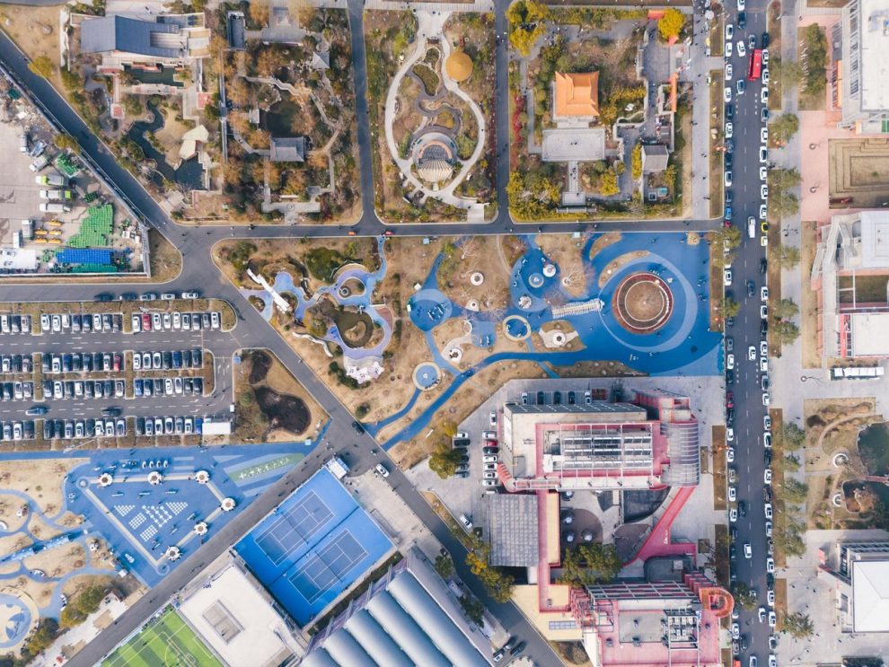 Vista aérea de um parque urbano com áreas de lazer, estacionamento e prédios ao redor
