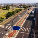 Vista aérea de uma via urbana com ciclovias, áreas verdes e circulação de veículos.