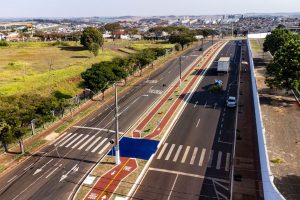 Vista aérea de uma via urbana com ciclovias, áreas verdes e circulação de veículos.