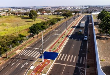 Vista aérea de uma via urbana com ciclovias, áreas verdes e circulação de veículos.