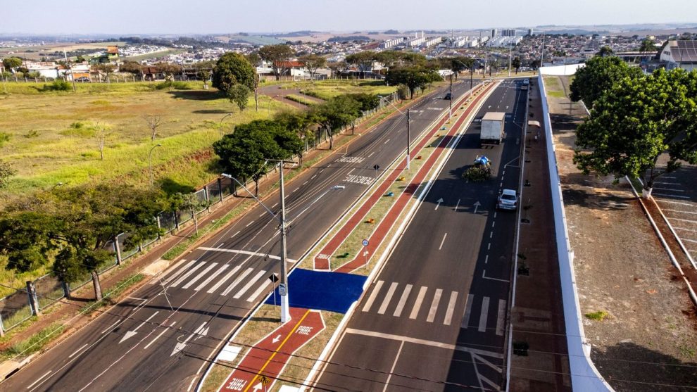 Vista aérea de uma via urbana com ciclovias, áreas verdes e circulação de veículos.