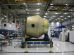 Equipamento espacial em construção sobre uma plataforma móvel dentro de uma fábrica aeroespacial.