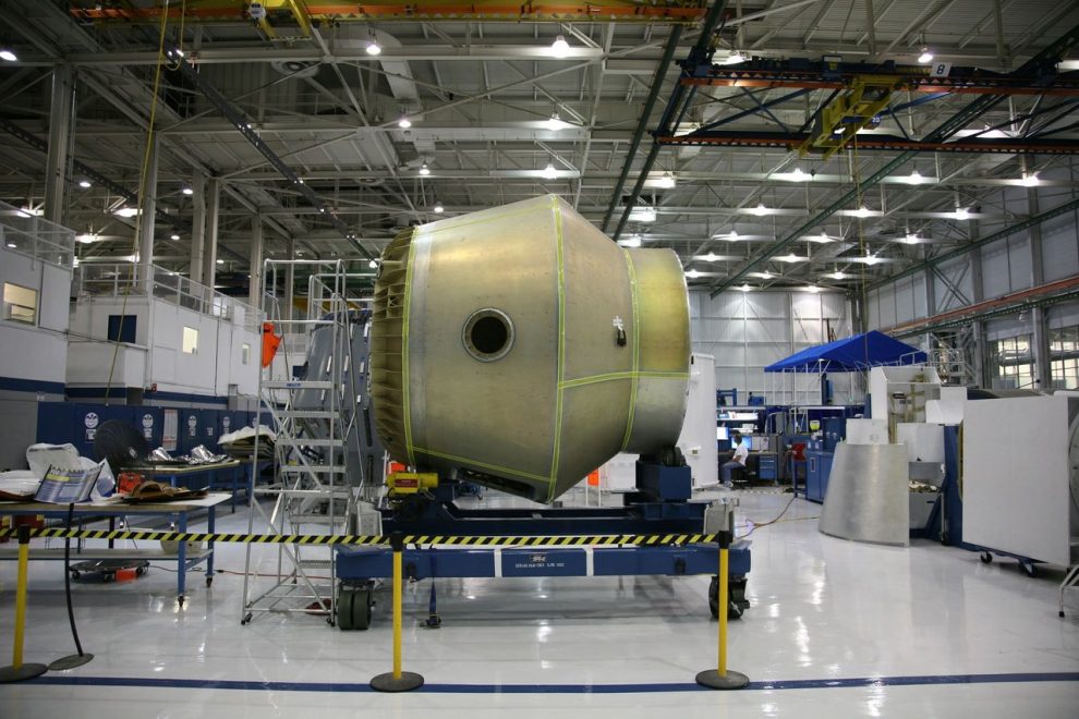 Equipamento espacial em construção sobre uma plataforma móvel dentro de uma fábrica aeroespacial.